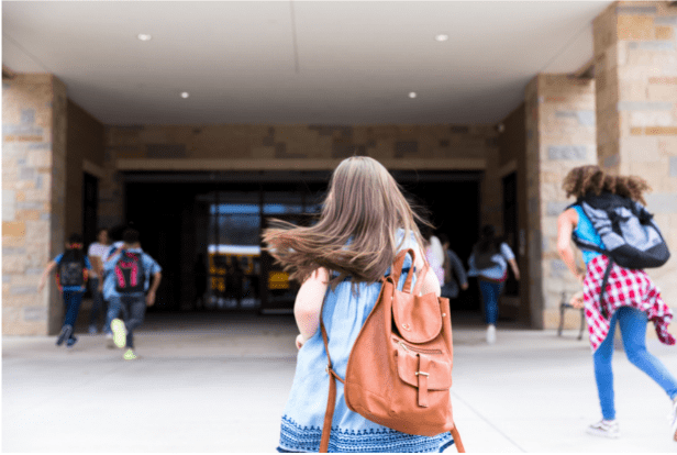 A middle school girl carries her backpack as she walks towards the school doors. 