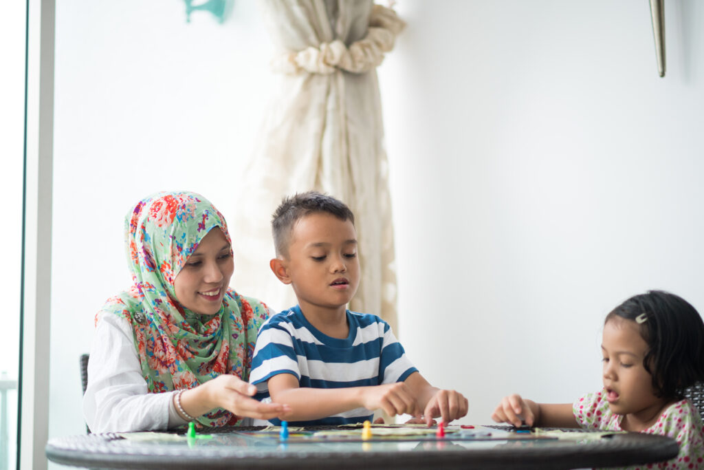 Muslim mom playing a board game with her young kids at home