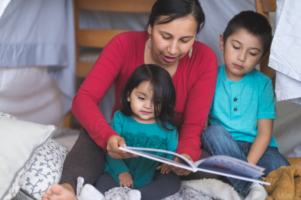 Mom reads with her two young children under makeshift fort in living room.