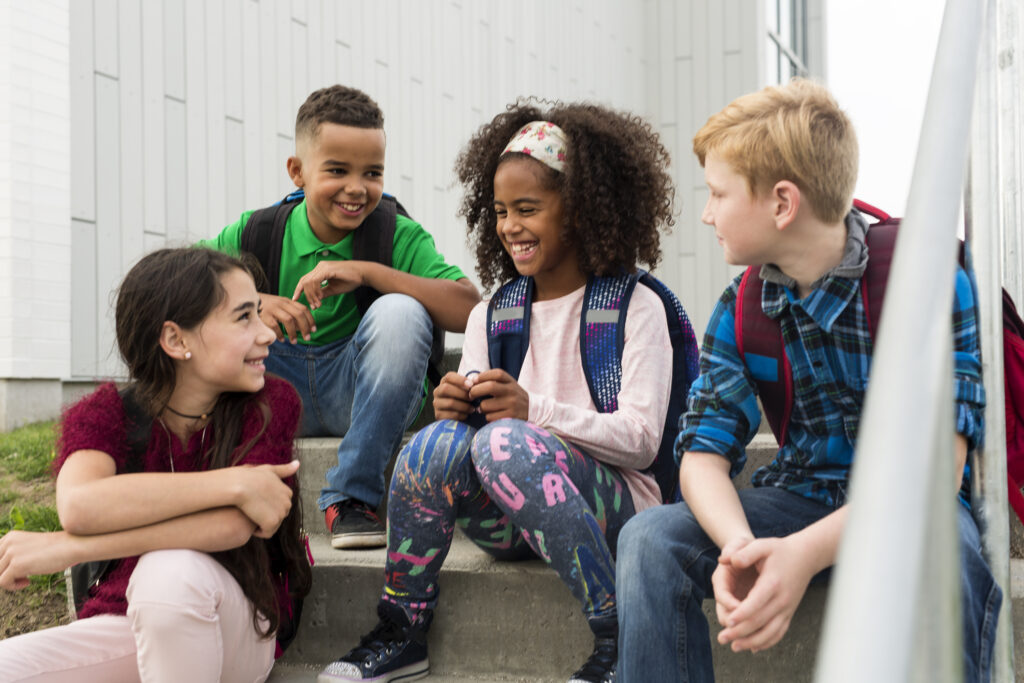 A multiethnic group of middle school students sit on stairs together talking with each other.