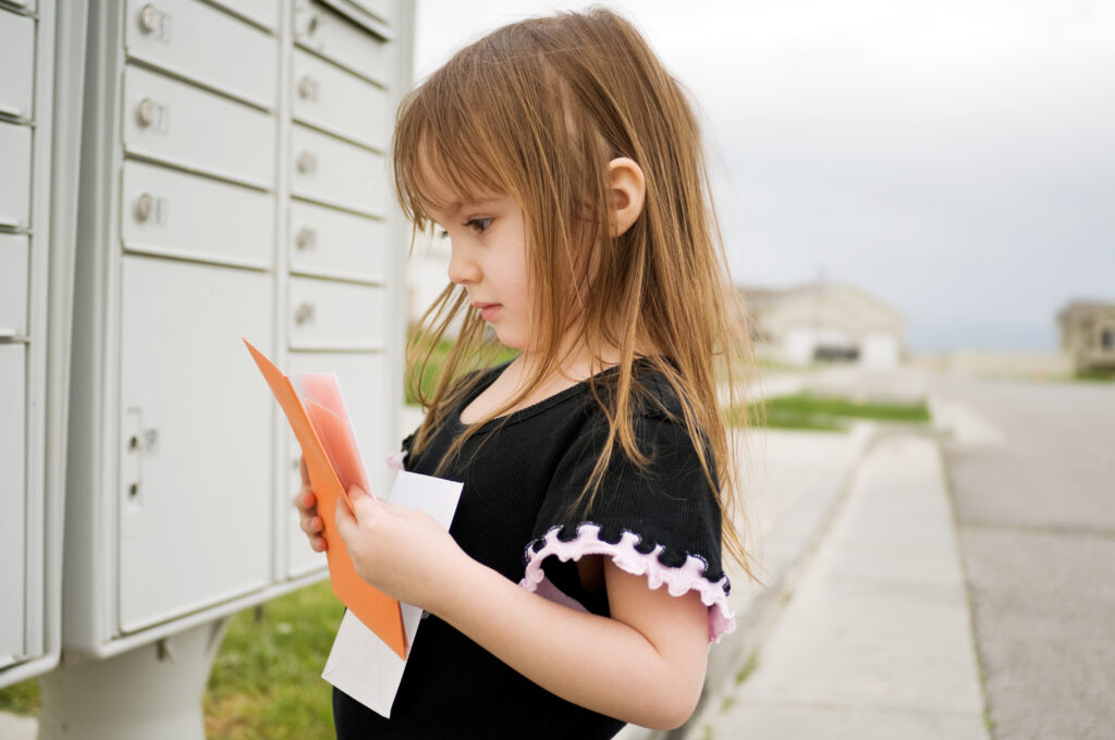 A young girl looks at letters from her mailbox on her neighborhood street.