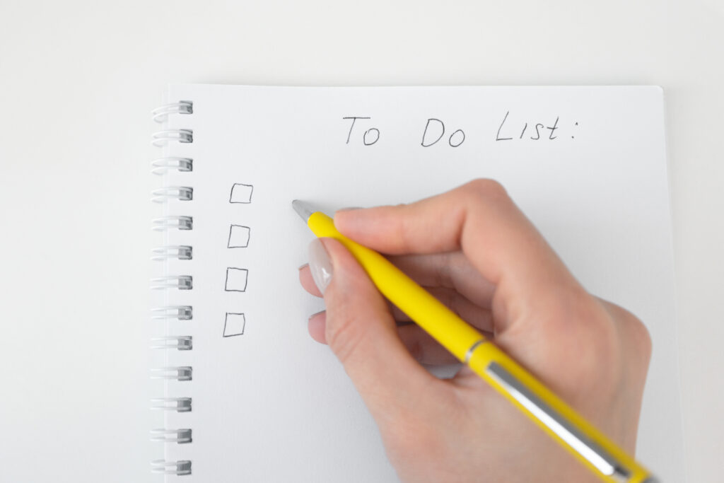 A woman's hand uses a pencil to write down tasks on her to-do list in a notebook.