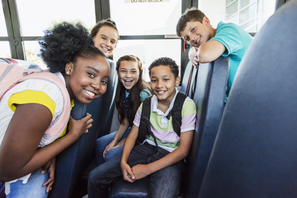 A group of multiethnic kids smiles while sitting on the school bus. 