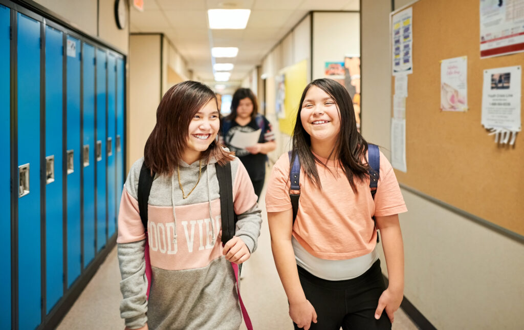 Two middle school students smiling and walking together down the hallway to class. 