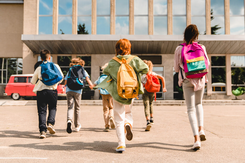 A group of middle school students run together with their backpacks to their school building.