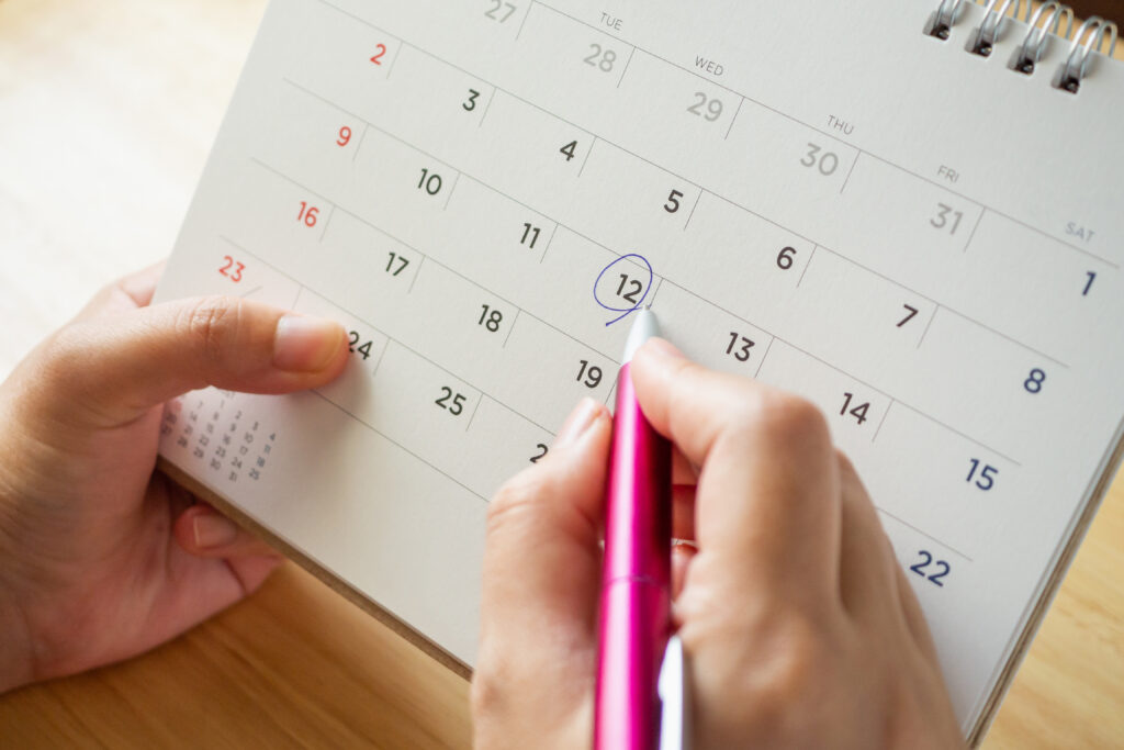 A woman holds a paper calendar and circles a date with a pencil. 