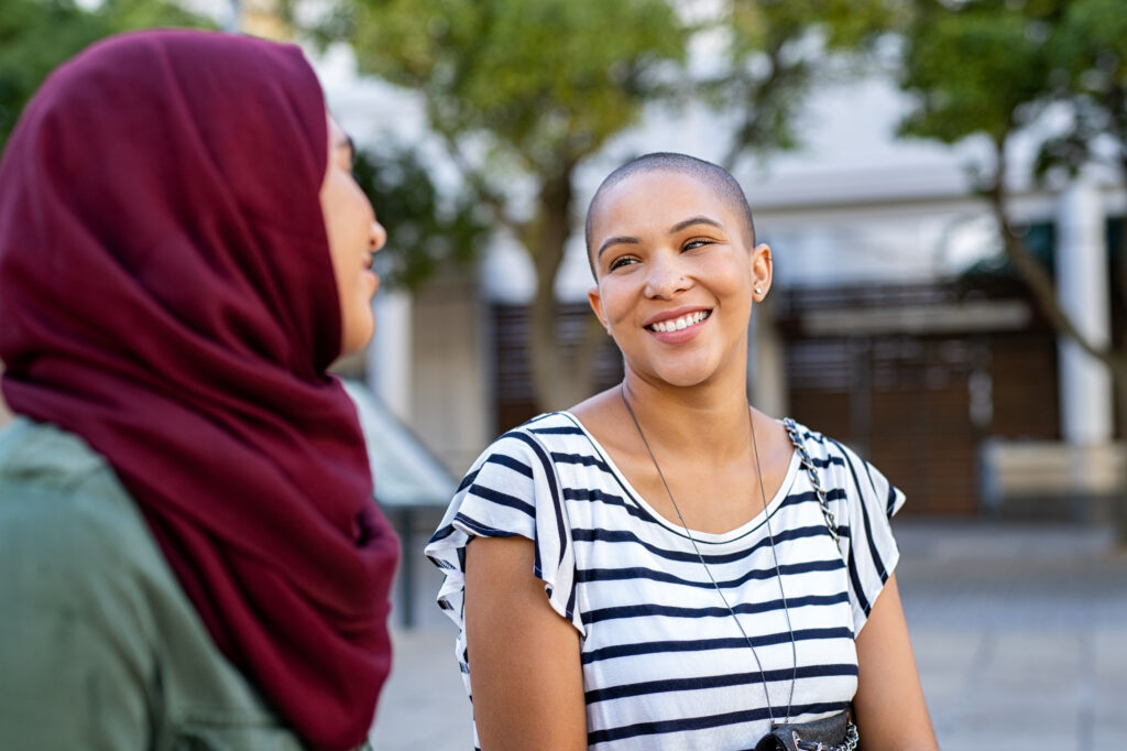 A smiling black woman talks with a smiling Muslim woman in the community.