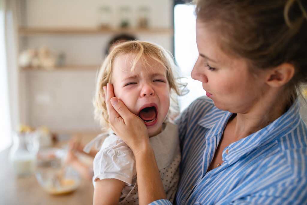 A concerned mother holds her crying toddler in their kitchen. 