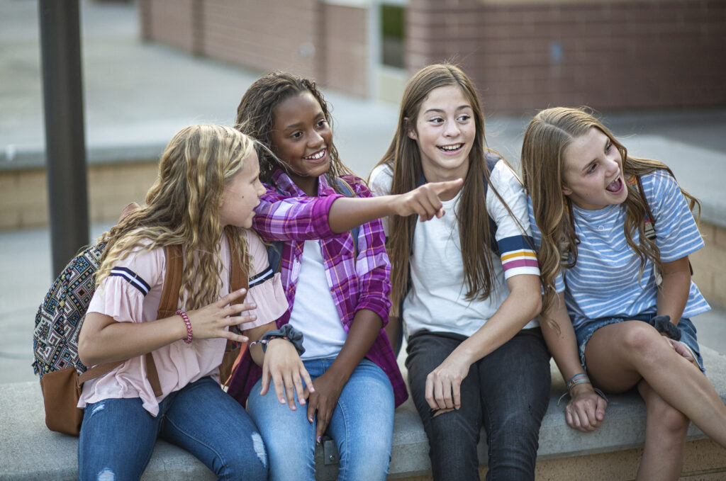 A multi-ethnic group of middle school girls smile and laugh together. 