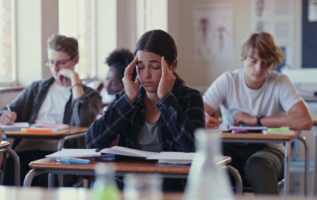 Stressed teen student puts her hands on her head as she sits in class. 