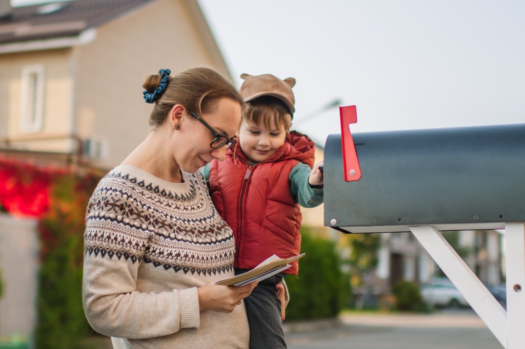 A mother and her young toddler retrieve mail from their mailbox in their neighborhood. 
