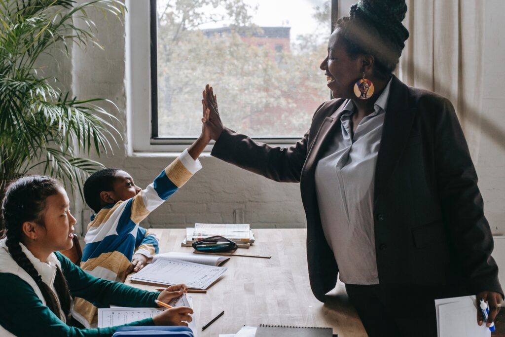 A black teacher gives her student a high-five as they work on their assignment.