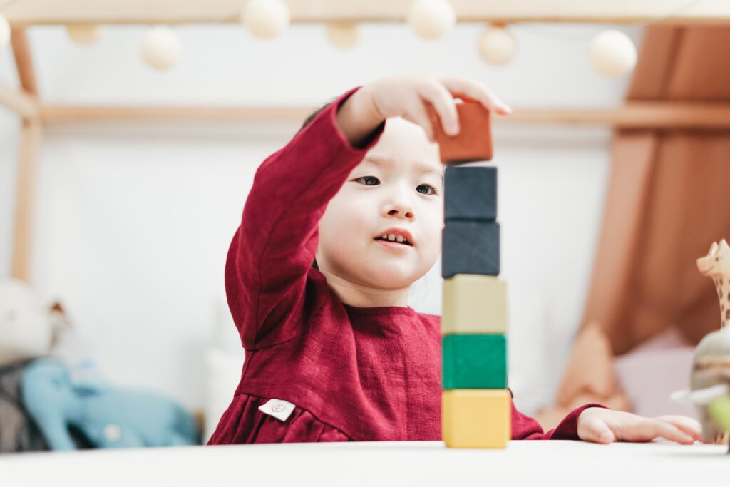 An Asian toddler stacks colorful blocks together at daycare.